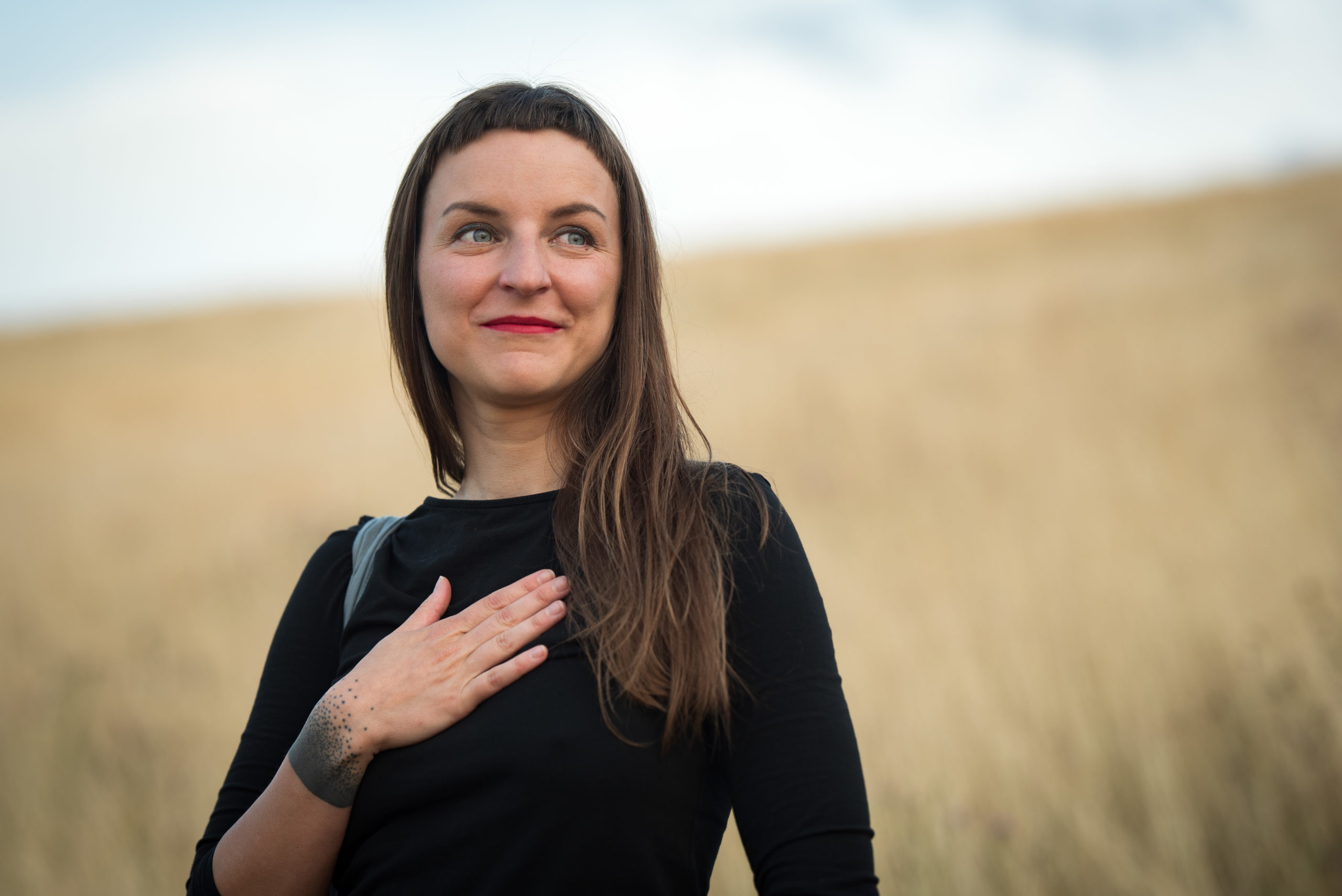 Žena v černém oblečení pociťující vděk s rukou na srdci.
